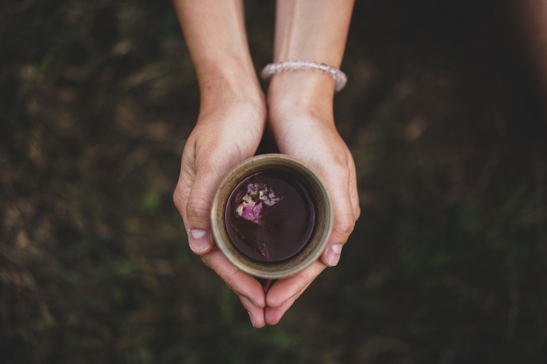 Two hands holding a cup of ceremonial cacao with rose petals